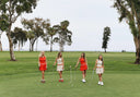 Four women in red and white outfits on a golf course with trees in the background