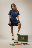 A model wearing the Golf Chalet Pleated Skirt in navy, paired with a matching polo. The skirt features a flattering, high-waisted pleated design ideal for comfort and style on the golf course.