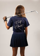 Back view of a woman wearing the Golf Chalet Polo in navy, featuring elegant embroidery, paired with a pleated skirt, perfect for both golf and casual outings.