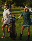 Two women wearing stylish outfits from the Loma Club Collection, showcasing modern women's golf apparel on the course with vibrant designs and performance features.