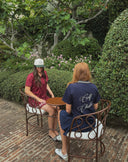 Two women in a serene garden setting, wearing The Palermo Collection by Henslowe, showcasing stylish women's golf apparel.