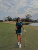 Woman in golf attire standing on a golf course with a scenic background