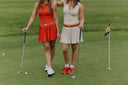 Two women on a golf course with golf clubs and a flag in the background.