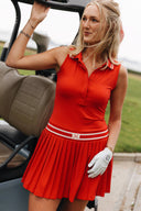 Woman in a red dress with a white glove standing next to a golf cart on a golf course.