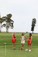 Three women on a golf course with trees in the background