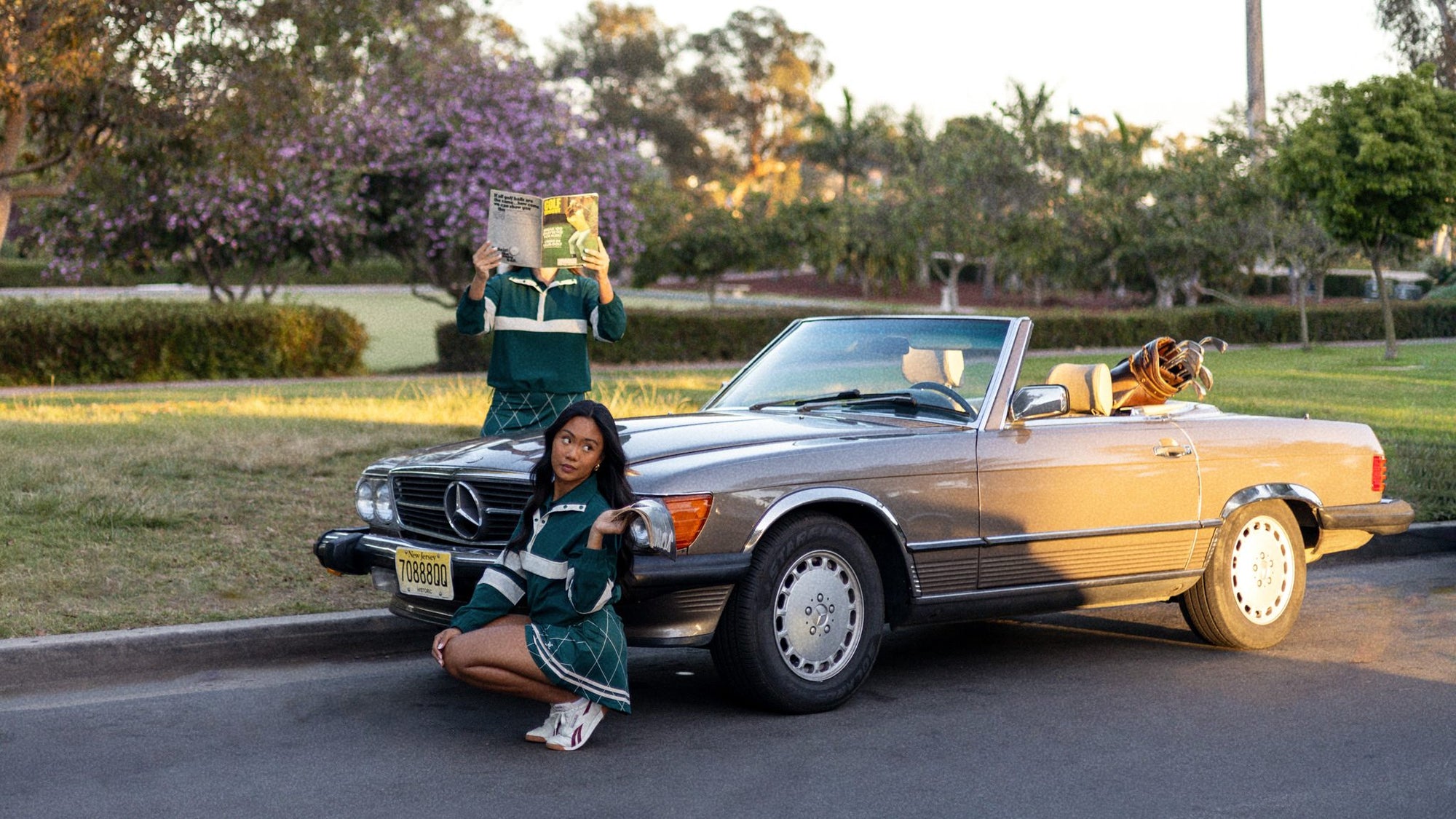 Woman taking a photo of another woman in front of a classic convertible car.